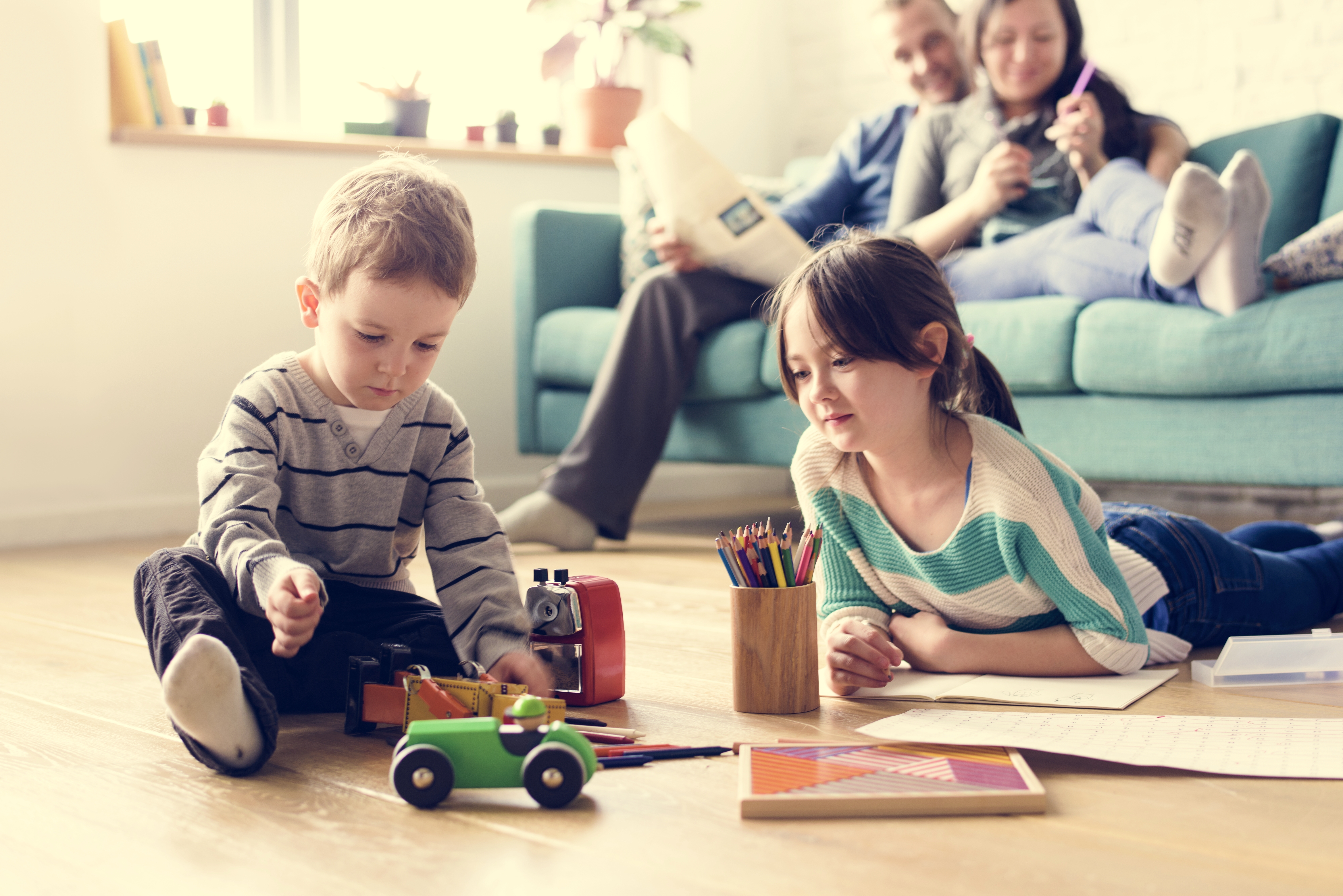 children on floor playing with toys, parents on sofa behind